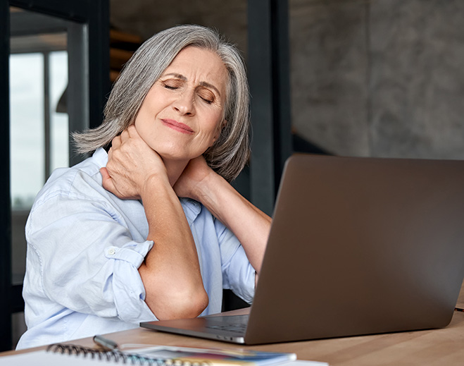 Person holding neck while using laptop