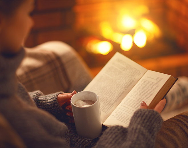 Person reading book by fireplace