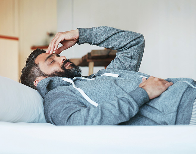Person lying in bed holding head