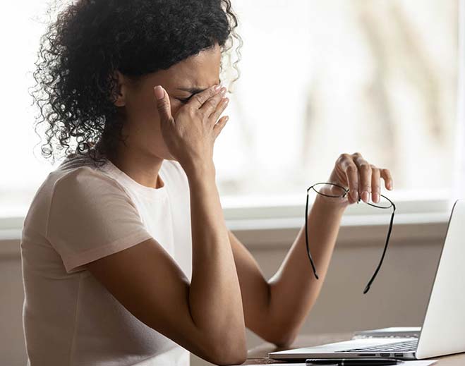 Person rubbing eyes while using laptop