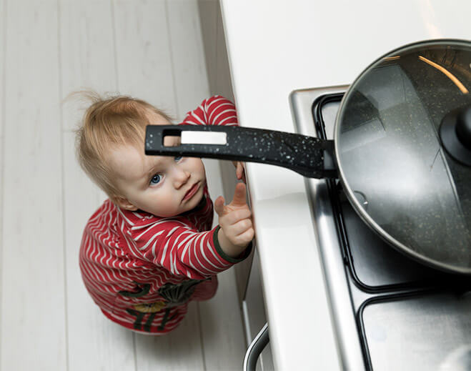 Child reaching toward stove handle in kitchen