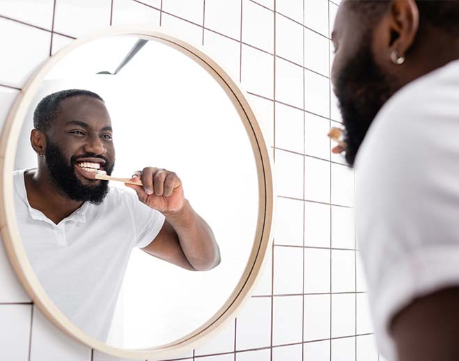 Person brushing teeth in bathroom mirror