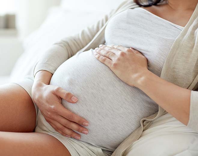 Pregnant person holding belly at home