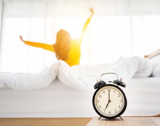 Person stretching in bed beside alarm clock
