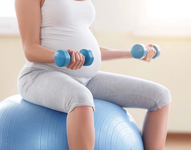 Pregnant person exercising with dumbbells on ball