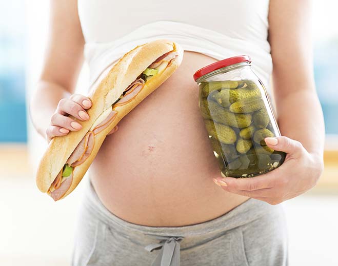 Pregnant person holding sandwich and pickles