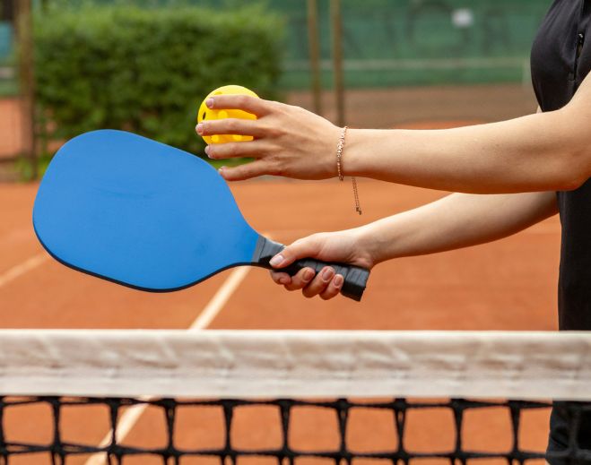 Person holding paddle and ball at net