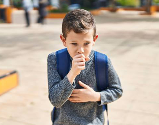 Child coughing outdoors with backpack