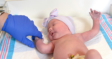 Healthcare worker holding newborn baby's hand