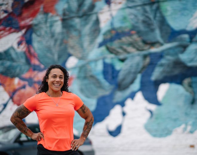 Jasmine in orange shirt standing before mural